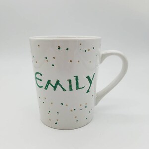 May include: White ceramic mug with a green and gold confetti pattern and the name "Emily" written in green.