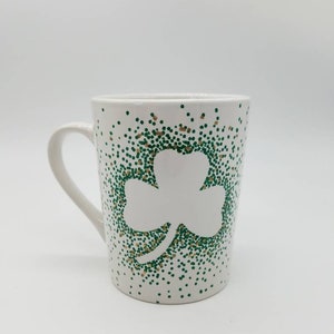 May include: White ceramic mug with a green and gold shamrock design. The shamrock is made of small dots.