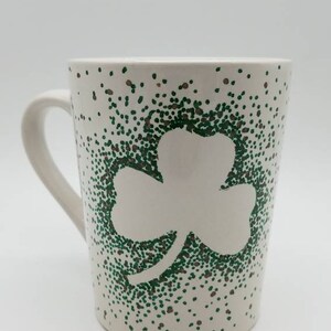 May include: White ceramic mug with a green shamrock design created with small dots. The shamrock is outlined in white.