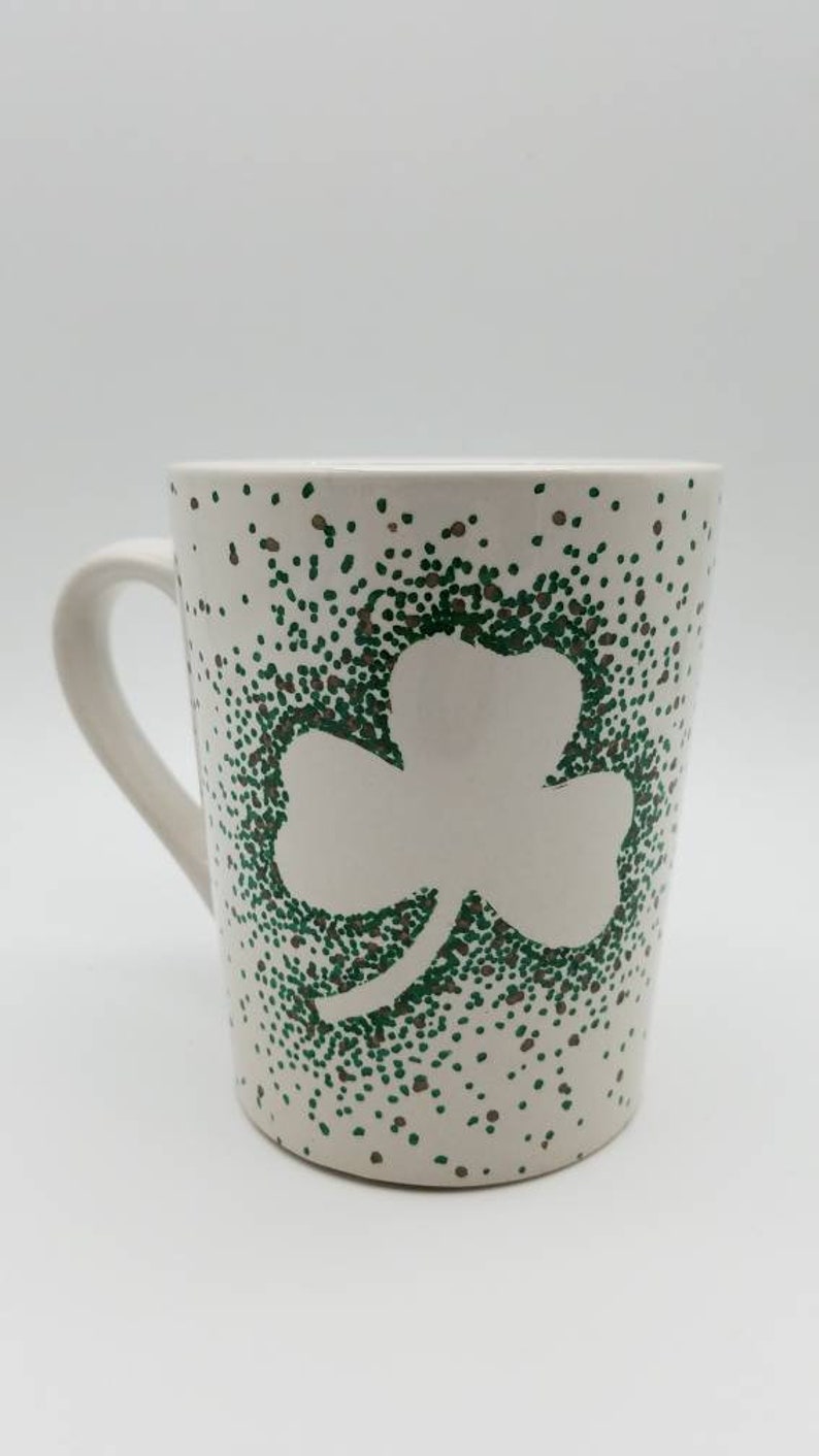 May include: White ceramic mug with a green shamrock design created with small dots. The shamrock is outlined in white.