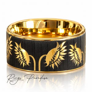 May include: A wide band ring featuring a brushed black exterior with a repeating pattern of gold-colored sunflower engravings. The interior of the ring is polished gold-colored metal. The text Rings Paradise is visible at the bottom of the image.