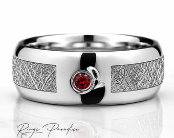 Peut inclure: Une bague argentée polie avec une pierre précieuse rouge ronde centrale sertie dans un chaton circulaire lisse. L'anneau présente deux panneaux rectangulaires avec une finition texturée et hachurée de chaque côté. Le texte Rings Paradise est visible.