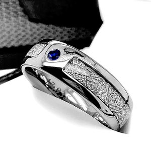 May include: A silver ring with a blue gemstone set in the center. The ring has a textured, brushed finish.