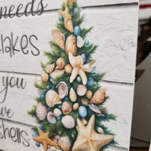 May include: A white wooden sign with a Christmas tree made of seashells and starfish. The sign reads "All you need is a little bit of beach to make you feel like you've got shells".