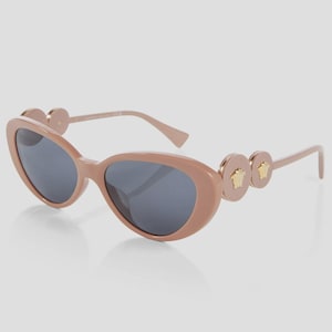 May include: Oval-shaped sunglasses in a light brown hue with dark gray lenses. The temples feature circular accents with gold-colored Medusa head emblems. A stylish accessory for eye protection.