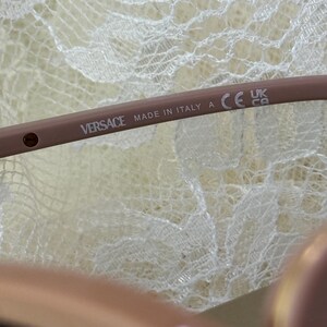 May include: Close-up of a light brown Versace eyeglass frame. The text "VERSACE MADE IN ITALY A" is printed on the frame. The frame also has a CE mark and a UK mark.