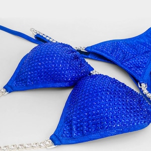 May include: A vibrant royal blue bikini top featuring triangular cups densely covered in matching blue crystals. The straps are adorned with clear, sparkling rhinestones set in silver-toned metal, providing a high-contrast, reflective finish.