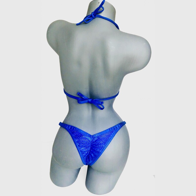 May include: A vibrant royal blue bikini set featuring a textured, shimmering fabric. The top has thin, adjustable tie straps at the neck and back, while the bottom is a high-cut style with a gathered center seam detail on the back panel.