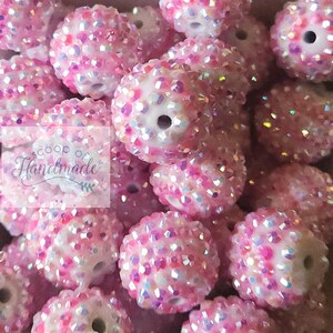 May include: A close-up of a pile of pink and white iridescent round beads. The beads are covered in small, sparkly crystals.