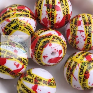 May include: Close-up of several white round beads with a red and yellow crime scene tape design. The beads have a glossy finish and are covered in red splatter paint.