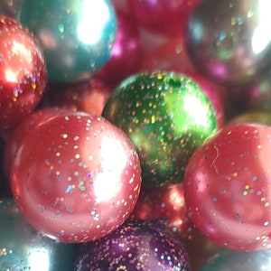 May include: A close-up of a collection of round, iridescent beads with glitter. The beads are in various shades of red, green, blue, and purple.