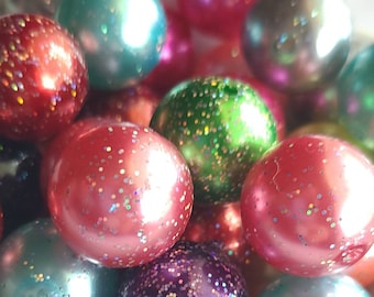 May include: A close-up of a collection of round, iridescent beads with glitter. The beads are in various shades of red, green, blue, and purple.