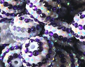 May include: Close-up of white iridescent round beads with purple rhinestones. The beads are clustered together and have a sparkly finish.