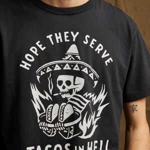Peut inclure: T-shirt noir avec un graphique blanc d'un squelette portant un sombrero et tenant deux tacos. Le texte "HOPE THEY SERVE TACOS IN HELL" est imprim&eacute; sous le graphique.