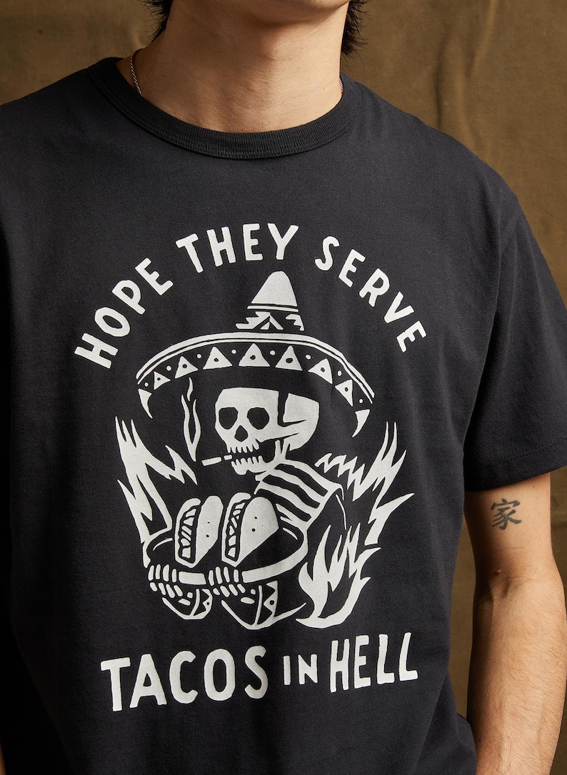 Peut inclure: T-shirt noir avec un graphique blanc d'un squelette portant un sombrero et tenant deux tacos. Le texte "HOPE THEY SERVE TACOS IN HELL" est imprim&eacute; sous le graphique.