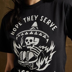 Peut inclure: T-shirt noir avec un graphique blanc d'un squelette portant un sombrero et tenant des tacos. Le texte "Hope they serve tacos in hell" est imprim&eacute; sous le graphique.