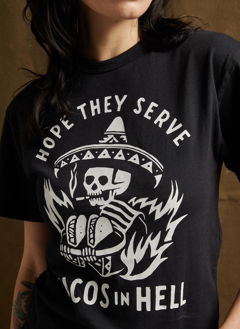 Peut inclure: T-shirt noir avec un graphique blanc d'un squelette portant un sombrero et tenant des tacos. Le texte "Hope they serve tacos in hell" est imprim&eacute; sous le graphique.