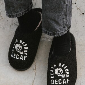 May include: A pair of black fuzzy slippers with a white skull and crossbones graphic and the text "Death Before Decaf".