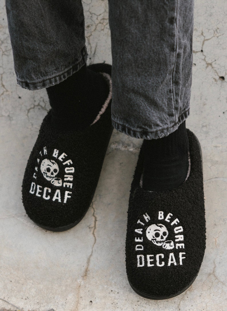 May include: A pair of black fuzzy slippers with a white skull and crossbones graphic and the text "Death Before Decaf".