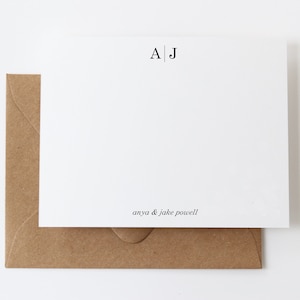May include: A white card with a brown envelope. The card has the initials "A|J" printed in black at the top and the text "anya & jake powell" printed in black at the bottom.