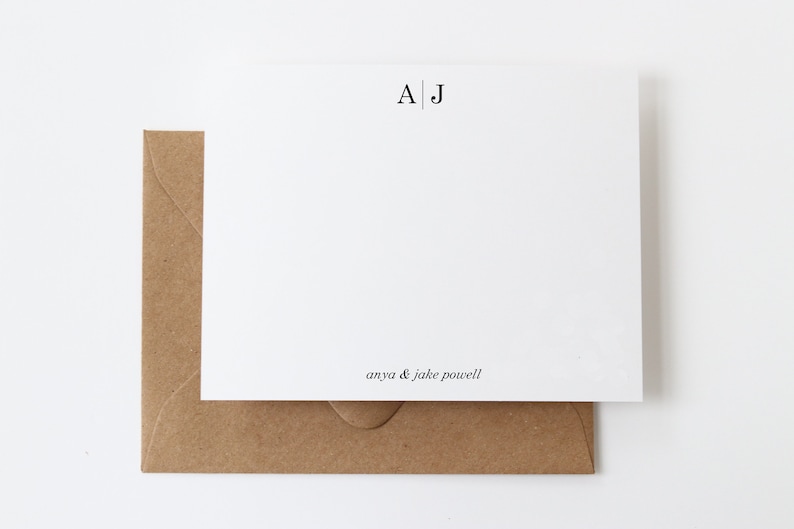 May include: A white card with a brown envelope. The card has the initials "A|J" printed in black at the top and the text "anya & jake powell" printed in black at the bottom.