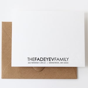 May include: A white card with black text reading "THEFADEYEVFAMILY" and an address, resting on a brown envelope. The card and envelope are on a white background. The envelope is made of a textured, brown paper.