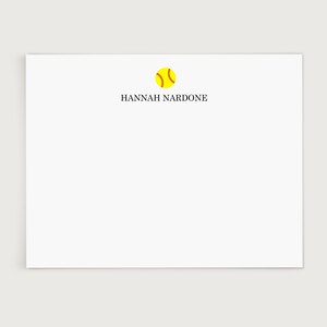 May include: A white stationery card with the name "HANNAH NARDONE" printed in black. A yellow softball graphic with red stitching is above the name. The card is rectangular and has a clean, minimalist design.