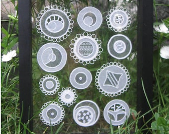 May include: A black framed picture with a glass front showcasing white lace circles of various designs. The title "Tanja Berlin" is printed at the top of the frame.