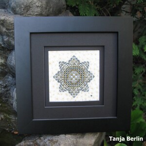 Könnte beinhalten: Ein schwarzer Bilderrahmen mit weißem Hintergrund und einem schwarzen und goldenen geometrischen Muster in der Mitte. Der Text "Tanja Berlin" befindet sich am unteren Rand des Bildes.