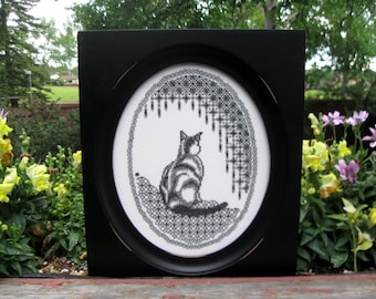 May include: Black and white embroidery of a cat sitting in a circle with a black and white lace design. The embroidery is framed in a black frame.