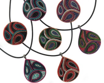 May include: Six pendants and brooches with intricate embroidered designs in shades of black, red, green, blue, and silver. The pendants are shaped like circles and teardrops and are strung on black cords. The text "TanjasHandEmbroidery" is visible at the bottom of the image.