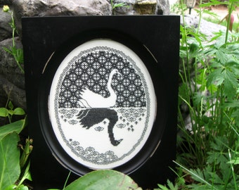 May include: Black and white embroidery of a swan in a black frame. The swan is depicted in a stylized design with a geometric pattern in the background.