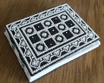 May include: A black and white needle case with a geometric design embroidered on the front. The case is titled "Hapsburg Lace Needle Case" and the maker's name is "Tanja Berlin".