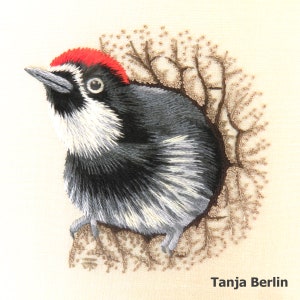 May include: Embroidered artwork of a black and white woodpecker with a red crown perched on a branch. The artwork is framed by a brown branch with small brown leaves.