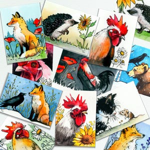May include: A collection of watercolor art prints featuring various animals including a fox, hedgehog, rooster, bear, cat, and mouse. The illustrations incorporate natural elements like sunflowers, poppies, daisies, and birds, rendered in vibrant colors.