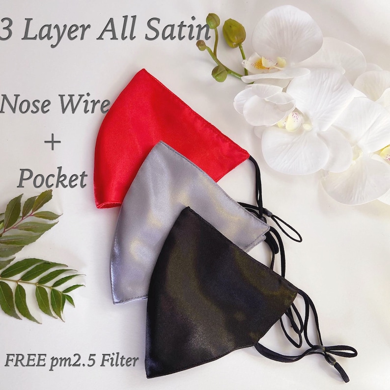Puede incluir: Tres mascarillas de sat&eacute;n en rojo, plateado y negro. Cada mascarilla tiene un alambre para la nariz y un bolsillo para un filtro. El texto "3 Layer All Satin", "Nose Wire + Pocket" y "FREE pm2.5 Filter" es visible en la imagen.