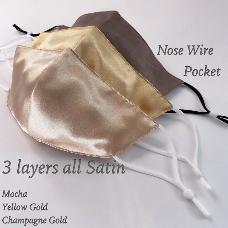 Puede incluir: Tres mascarillas de sat&eacute;n en tonos moca, oro amarillo y oro champ&aacute;n. Cada mascarilla tiene un alambre para la nariz y un bolsillo para un filtro. El texto "3 capas todo sat&eacute;n" est&aacute; impreso debajo de las mascarillas. El texto "Mocha", "Oro amarillo" y "Oro champ&aacute;n" est&aacute; impreso debajo del texto "3 capas todo sat&eacute;n".