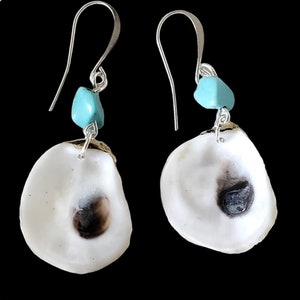 Könnte beinhalten: Handgefertigte Ohrringe mit natürlichen Austernschalen mit dunkelbraunem Zentrum, akzentuiert durch kleine türkisfarbene Perlen und silberfarbene Ohrhaken. Präsentiert vor schwarzem Hintergrund.