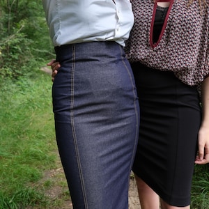 May include: Two women wearing skirts. One woman is wearing a white button-down shirt and a dark blue denim skirt. The other woman is wearing a red and black patterned blouse and a black skirt.