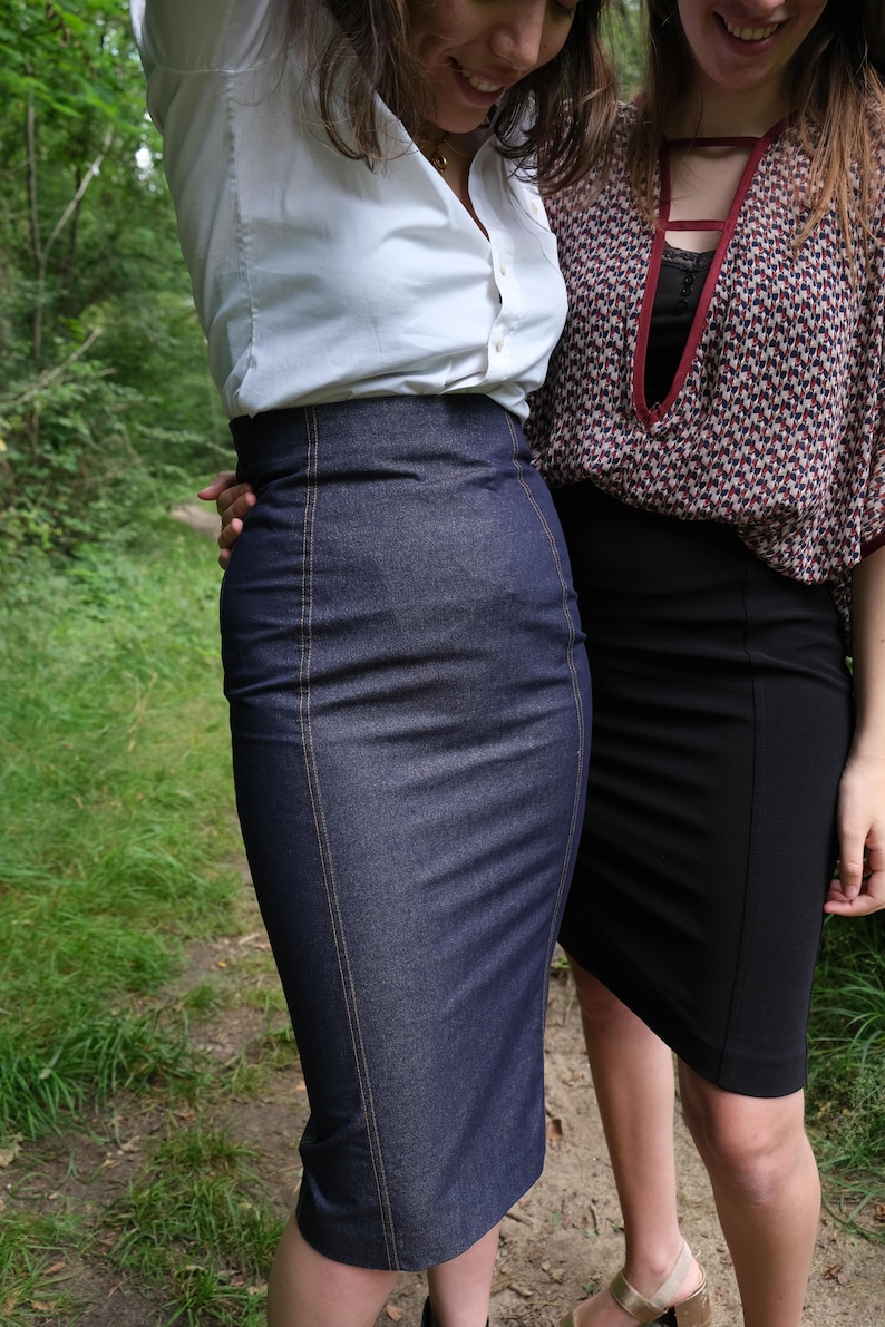 May include: Two women wearing skirts. One woman is wearing a white button-down shirt and a dark blue denim skirt. The other woman is wearing a red and black patterned blouse and a black skirt.