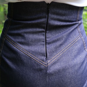 May include: A dark blue denim skirt with a zipper closure in the back. The skirt has a high waist and a fitted silhouette.