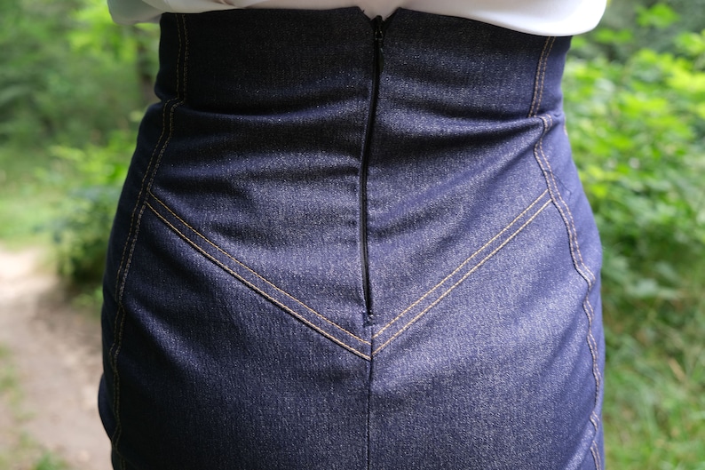 May include: A dark blue denim skirt with a zipper closure in the back. The skirt has a high waist and a fitted silhouette.