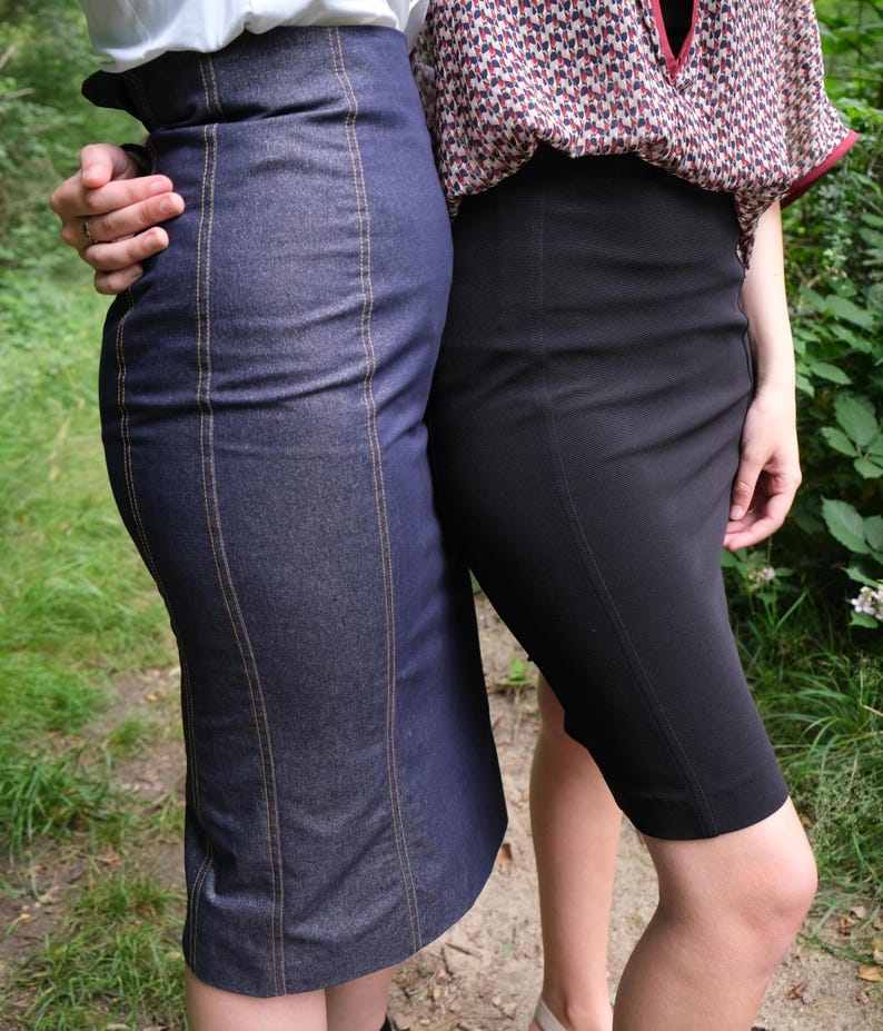 May include: Two women wearing skirts. One is wearing a dark blue denim skirt with gold stitching. The other is wearing a black skirt. Both skirts are knee-length and fitted.