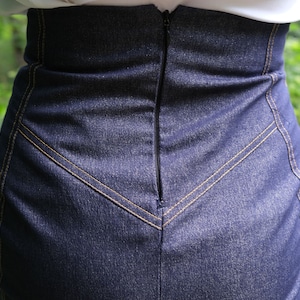 May include: A dark blue denim skirt with a zipper closure in the back. The skirt has a high waist and a fitted silhouette.