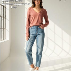 Peut inclure: Un t-shirt à manches longues rose poudré avec col en V et ouvertures pour les pouces, porté avec un jean bleu clair et des baskets blanches. Le texte sur l'image indique : PDF + Tutoriel T Shirt manches longues avec pouces apparents T46.