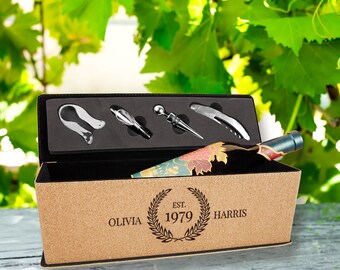 Puede incluir: Un juego de regalo de vino en una caja de corcho con interior negro, que contiene una botella de vino y cuatro herramientas de vino de acero inoxidable. La caja está personalizada con el texto "OLIVIA HARRIS EST. 1979". La botella de vino tiene una etiqueta decorativa.