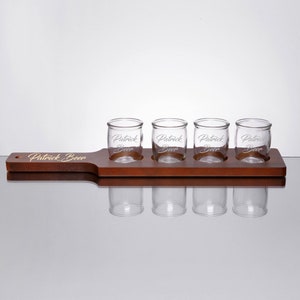 May include: A wooden beer flight tray with four small glasses. The tray is engraved with the text "Patrick Beer".