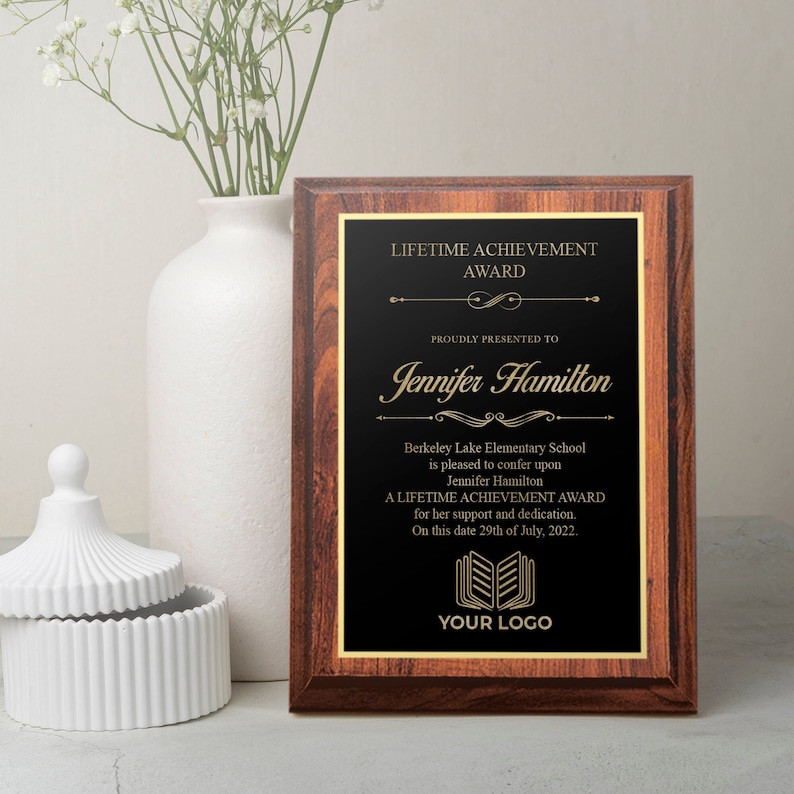 May include: A wooden plaque with a black background and gold lettering. The plaque reads "Lifetime Achievement Award" and is presented to Jennifer Hamilton. The plaque also includes the name of the school, Berkeley Lake Elementary School, and the date of the award, July 29th, 2022.