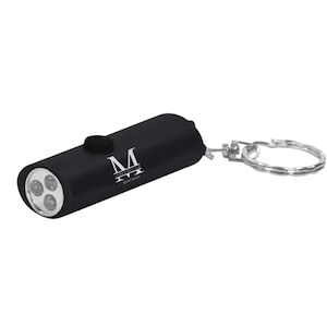May include: Black keychain flashlight with a silver key ring. The flashlight has four LED lights and is engraved with the text "M James Muller Bestman".