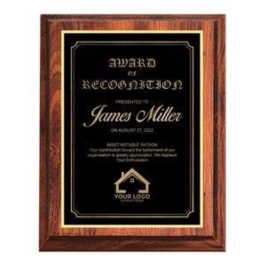 May include: A black and gold award plaque with a wooden frame. The plaque reads "Award of Recognition" presented to "James Miller" on August 27, 2022. The plaque also states "Most Notable Patron" and includes a logo with the text "Your Logo" and "Slogan Here".